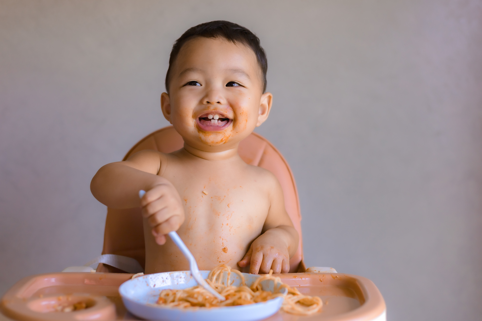 Asian boy eatting on high baby chair.